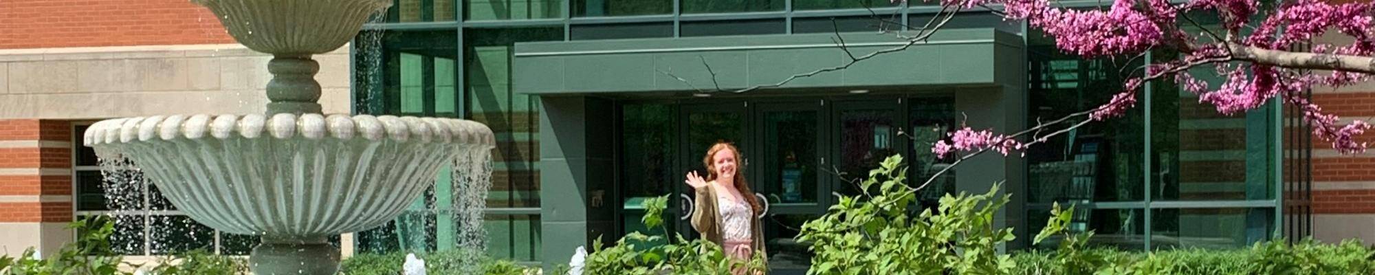 Student waiving next to the water fountain and flower blooming trees.